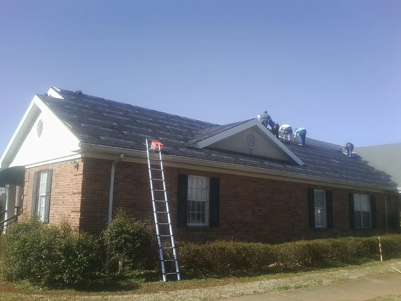 Crew tearing shingles off a brick ranch roof with a ladder set — Emergency Roof Repair work by our crew in Cedar Grove