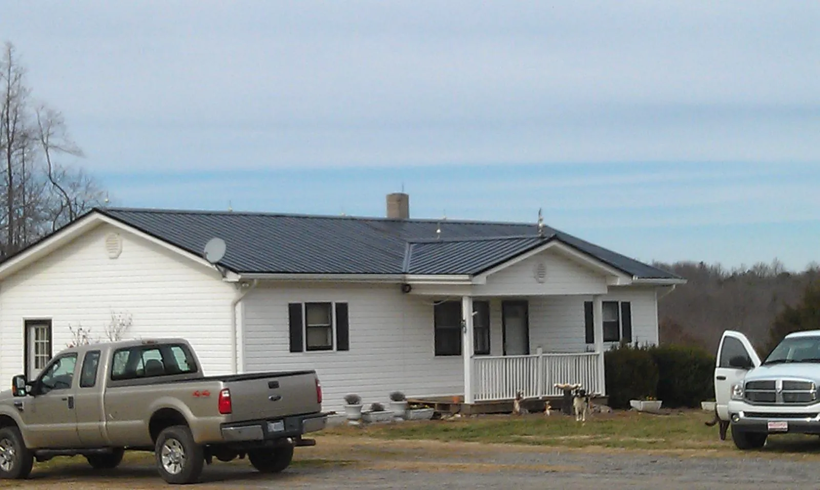 Finished dark metal roof on a white ranch home with work trucks parked in Cedar Grove