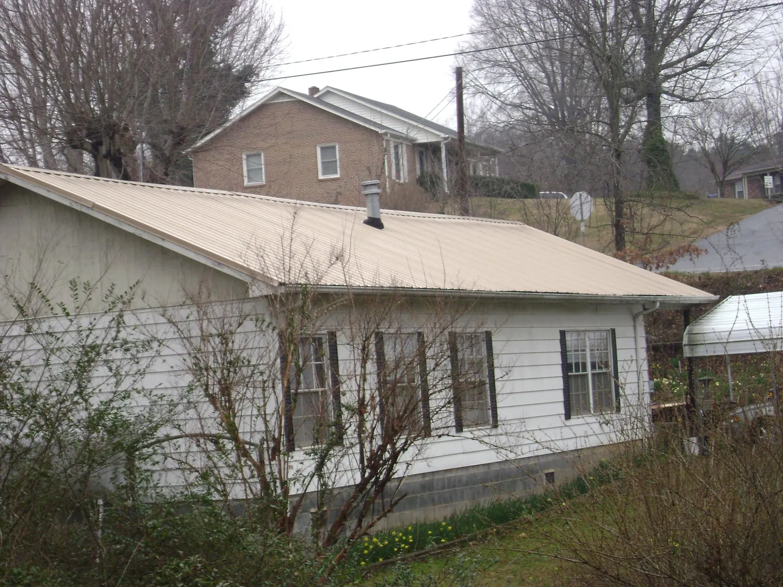 Tan metal roof on a white sided house set into a hillside — Commercial Roofing by Roofing Brothers in Cedar Grove